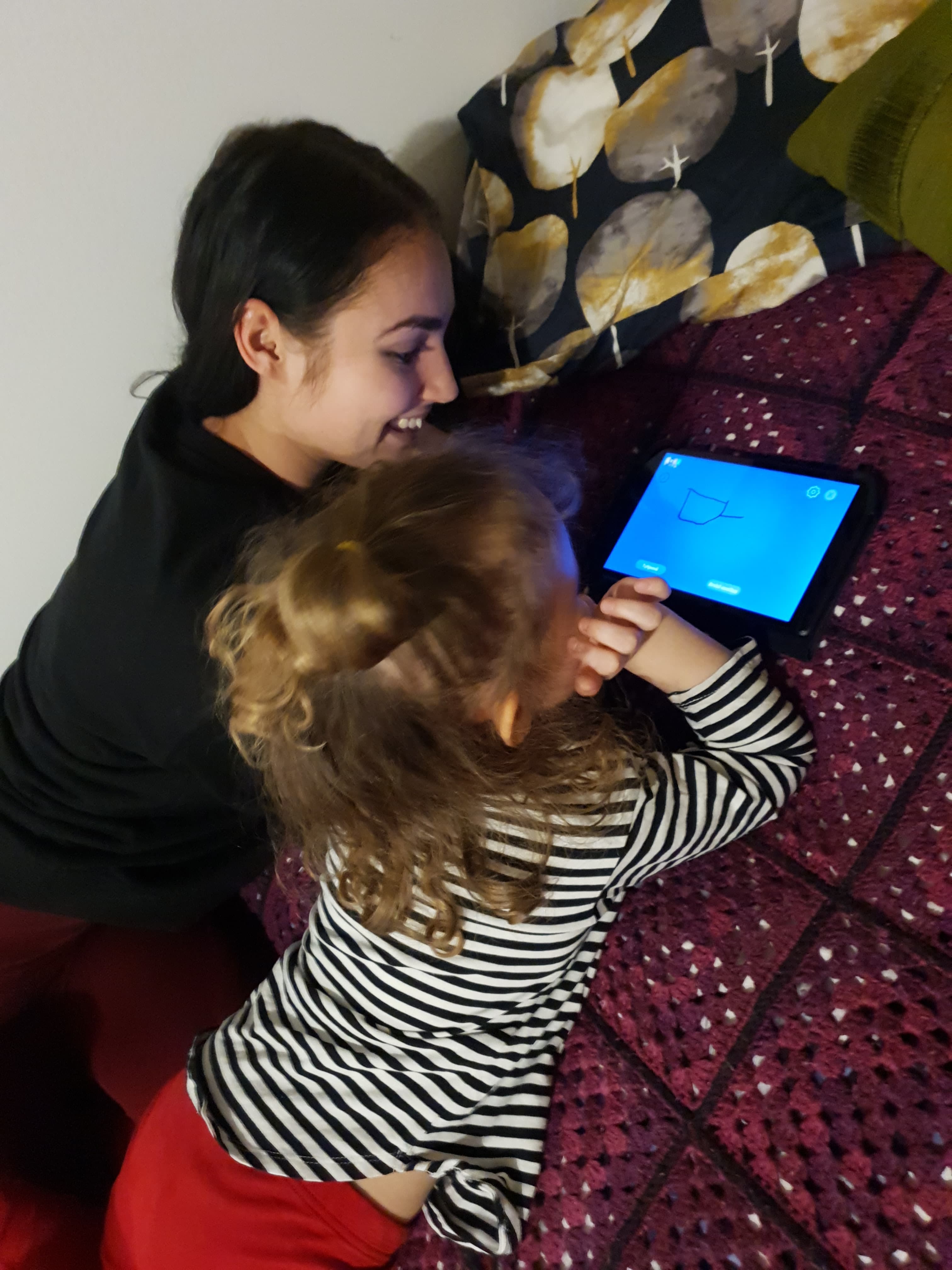 Aikuinen ja lapsi tabletilla maaten
